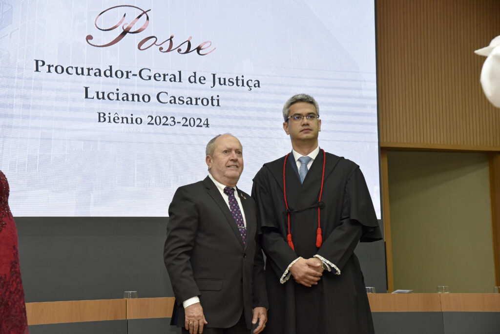 Na imagem, o procurador-geral de justiça, Eduardo Nicolau, vestindo terno escuro, ao lado do procurador-geral de justiça do Ministério Público do Tocantins, Luciano Casaroti, que veste beca. Ao fundo, um painel no qual se lê Posse Procurador-Geral de Justiça Luciano Casaroti Biênio 2023-2024
